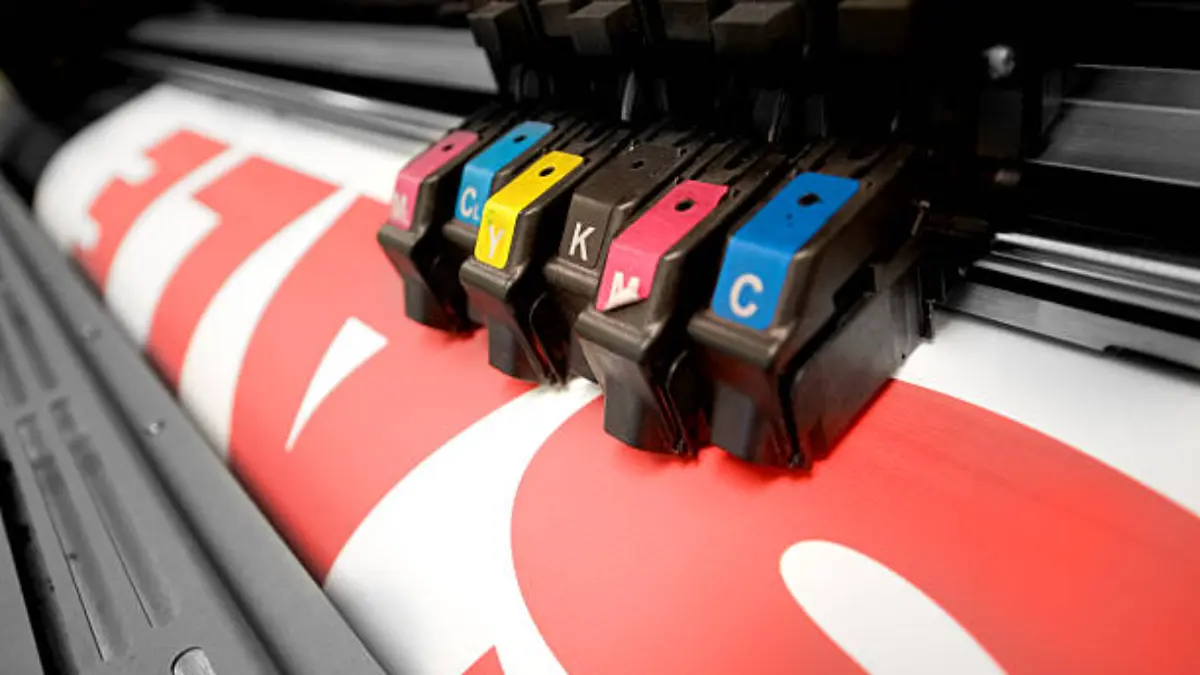 Inkjet print heads labelled in magenta, cian, yellow and black printing onto a roll of stock