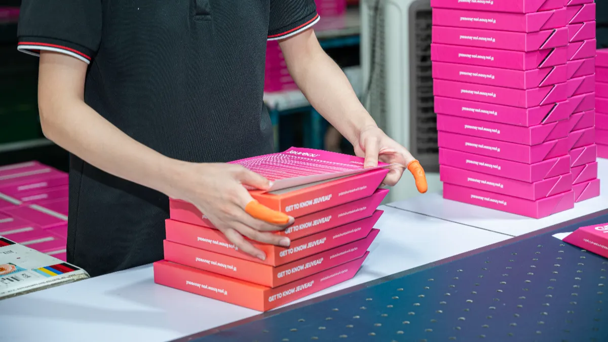 Worker stacking printed pink card boxes at a packaging assembly table