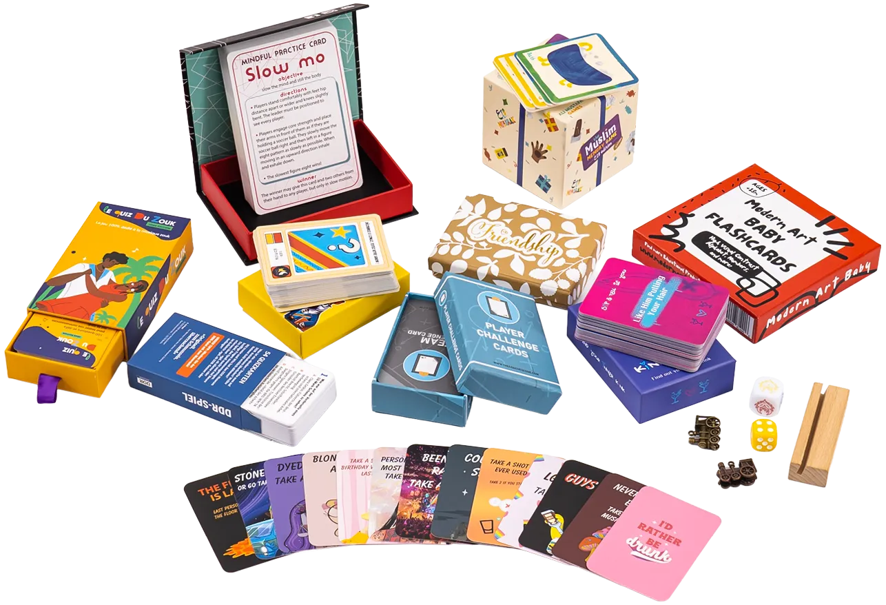 Open board game box with a rulebook, several colored card decks, punch tokens, dadi, and meeples laid out on a white surface