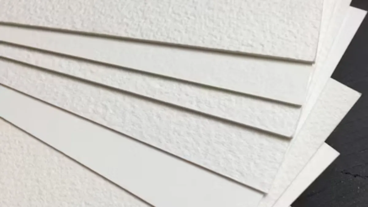 Corners of stacked white textured card sheets fanned to show their cut edges